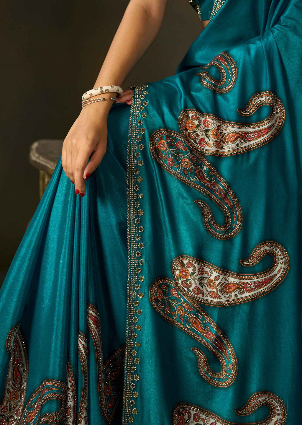 Close-up of firozi satin silk saree fabric showcasing intricate paisley motifs and embellished border.