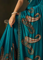 Close-up of firozi satin silk saree fabric showcasing intricate paisley motifs and embellished border.