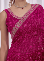 A close-up of a woman wearing a bright magenta pink saree with intricate silver and gold embroidery and a matching embroidered blouse.