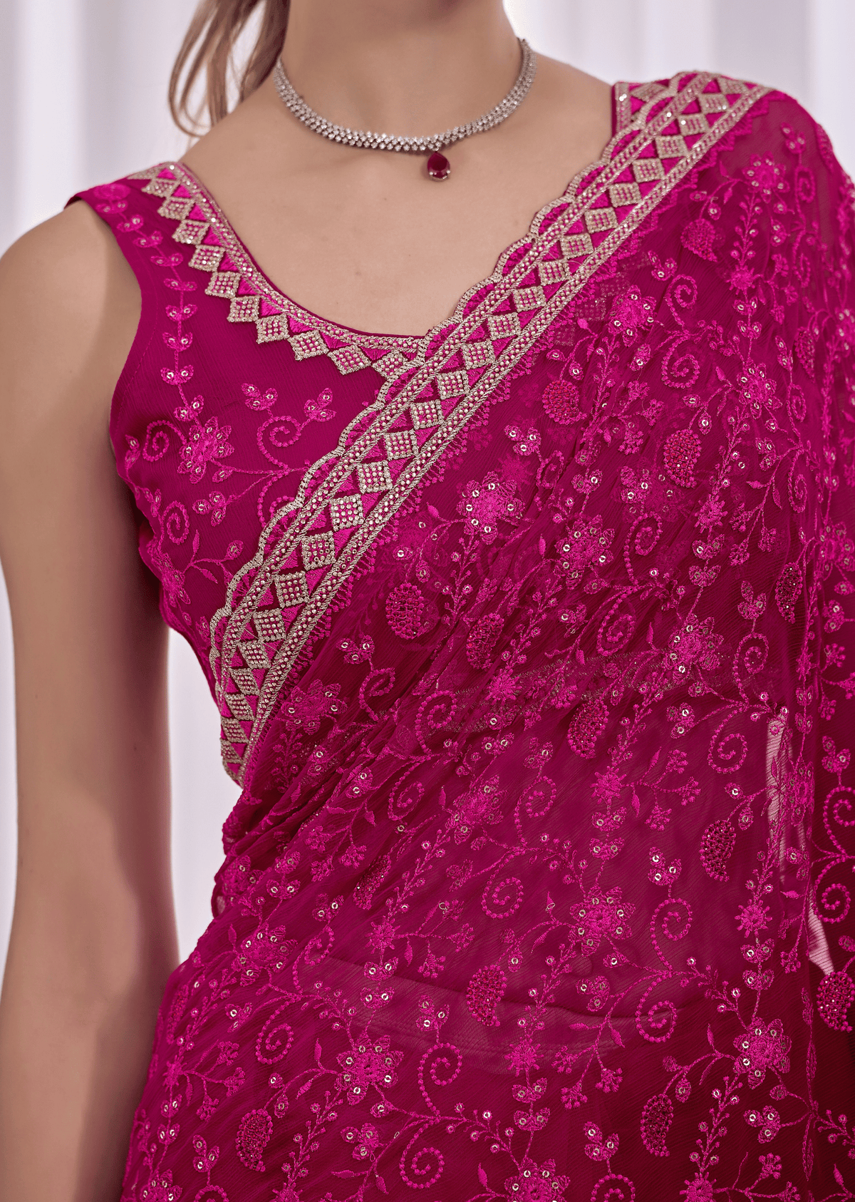 A close-up of a woman wearing a bright magenta pink saree with intricate silver and gold embroidery and a matching embroidered blouse.