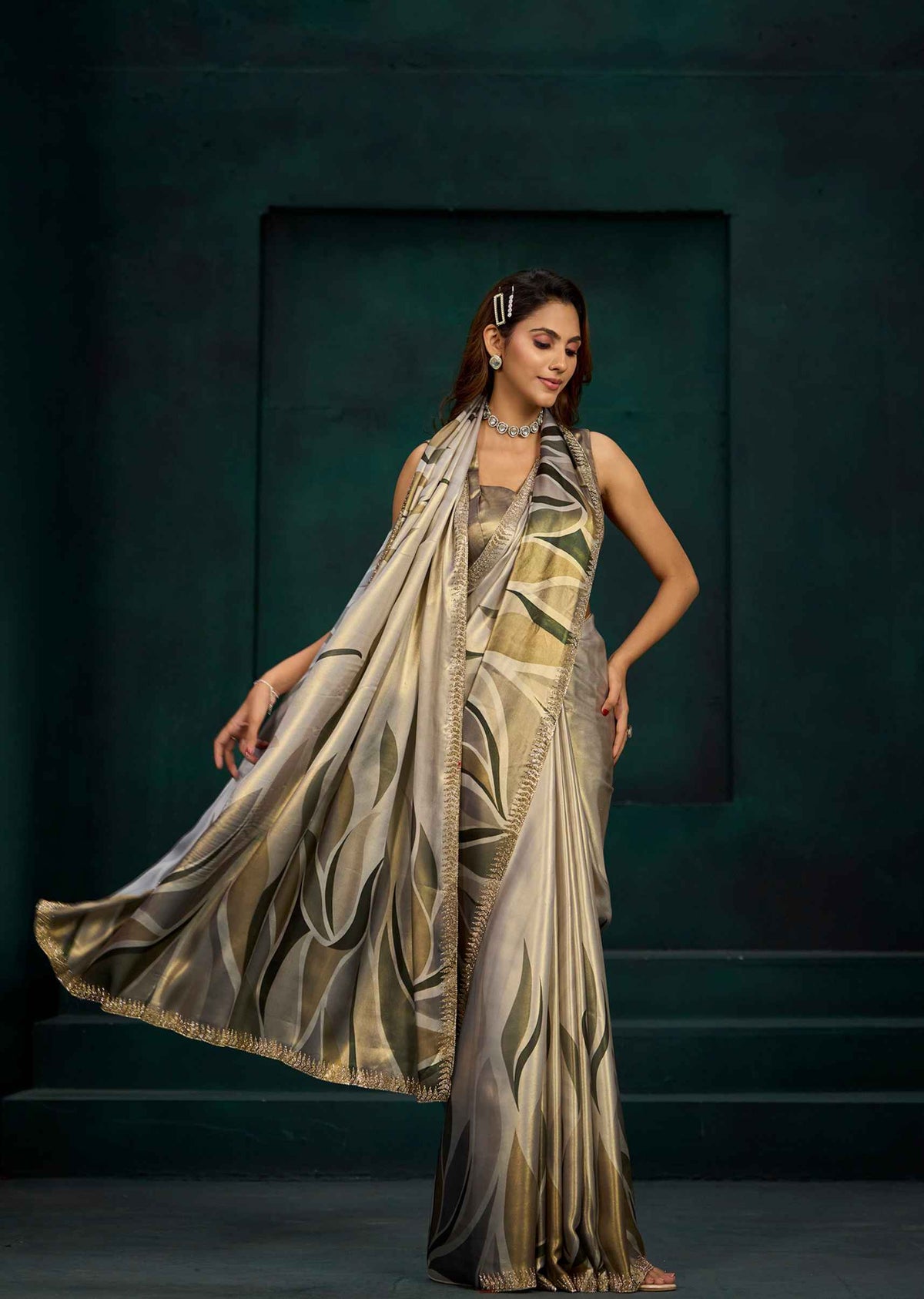 A woman models a metallic gold and silver saree with a matching dupatta against a dark teal studio backdrop.