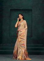 A woman models a draped saree with a metallic champagne-gold base and an abstract leaf-like pattern in bronze, brown, and orange tones, set against a dark green textured studio backdrop.