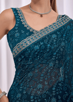 A close-up of a model wearing a dark teal blue saree with intricate silver and gold floral embroidery and a matching embroidered blouse.