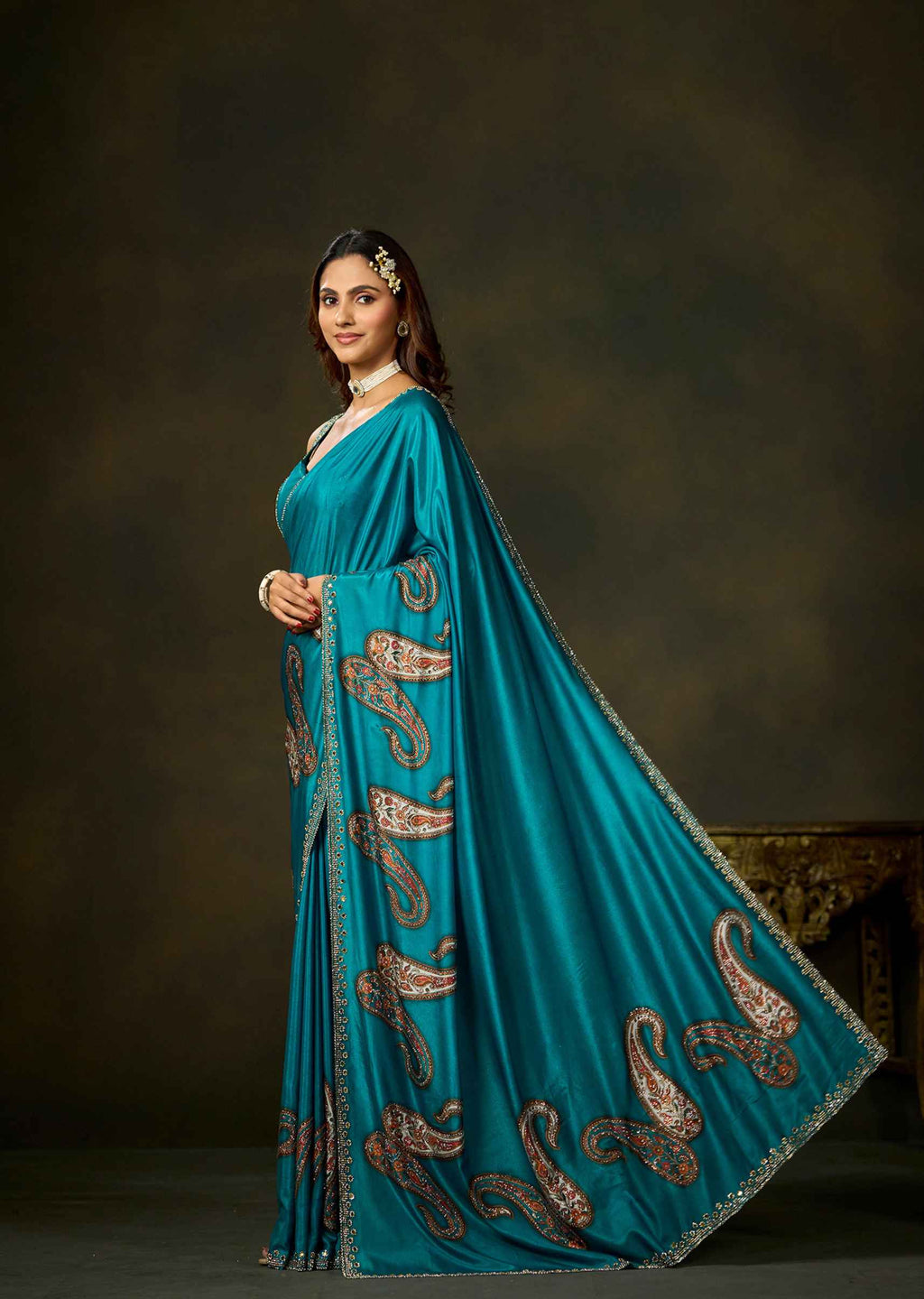 Firozi satin silk saree with intricate paisley motifs on the flowing pallu and embellished border.