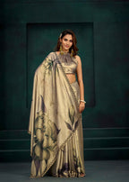 A woman models a beige and black floral printed saree with a matching metallic beige crop top against a dark green textured studio backdrop.