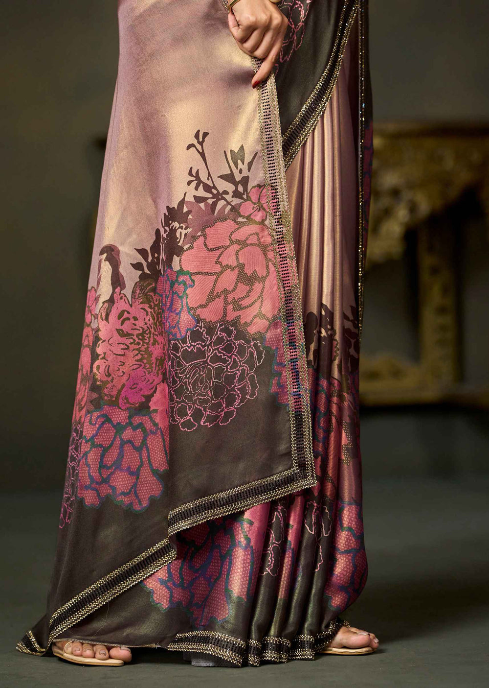 A close-up of a draped saree with a floral print in pink, magenta, and dark brown, paired with matching pleated fabric and a decorative border, shown on a model.