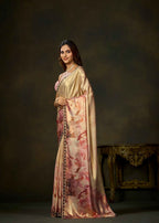 A woman modeling a traditional Indian saree in a studio setting. The saree has a shiny beige-gold body with a pink and red floral print on the lower portion and a dark patterned border.
