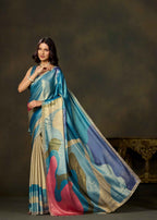 A woman models a luxurious blue and beige silk saree with abstract pink, blue, and gold patterns, posed against a dark brown studio backdrop.