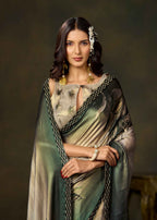 A woman modeling a traditional Indian saree with a green and beige floral print, paired with a matching dupatta and gold jewelry, set against a dark, textured studio background.