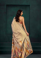 A woman is shown from behind wearing a draped beige saree with a multicolor abstract leaf pattern in orange, pink, and brown, set against a dark green textured studio background.