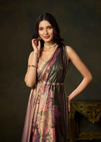A woman models a sleeveless, V-neck dress with a metallic bronze sheen and a pink floral print, styled with gold jewelry against a dark, elegant background.