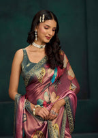 A woman wearing a floral-printed pink saree with a matching sleeveless blouse, styled with traditional jewelry against a dark green background.