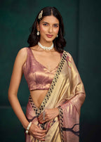 A woman modeling a metallic rose pink and gold saree with black geometric border detailing, set against a dark green studio background.