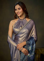 A woman modeling a shimmering lavender-purple halter-neck saree with a blue patterned pallu and gold zari borders, set against a dark brown studio background.