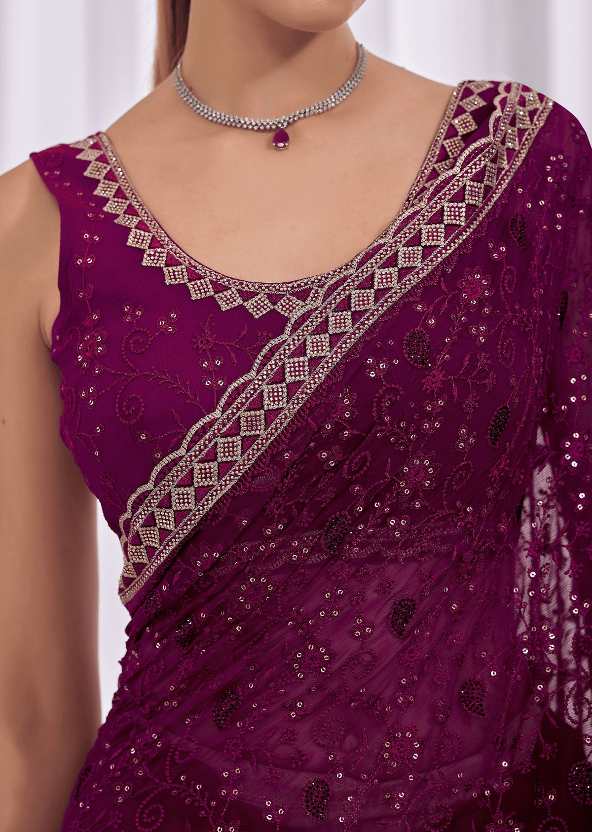 A close-up of a woman wearing a deep magenta purple embroidered saree blouse with silver mirror work and a matching draped saree.