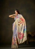 A woman models a draped silk saree with a multicolor abstract floral print on a dark brown studio background.