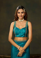 Woman wearing firozi satin silk saree with paisley detailing and matching blouse, upper body view.