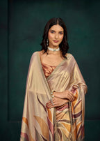 A woman modeling a shimmering champagne beige saree with abstract orange, brown, and mauve leaf-like patterns and a metallic gold border, set against a dark green studio backdrop.