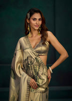 A woman modeling a metallic champagne-gold saree with black floral and geometric patterns, paired with a matching metallic blouse, set against a dark green studio background.