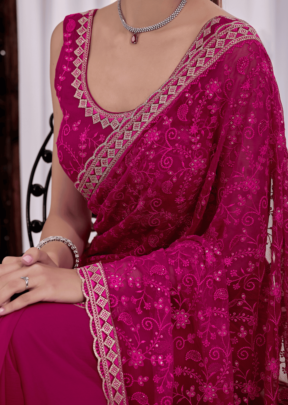 A close-up of a woman wearing a bright magenta pink saree with intricate silver and gold embroidery, featuring a matching embroidered sleeve and blouse.