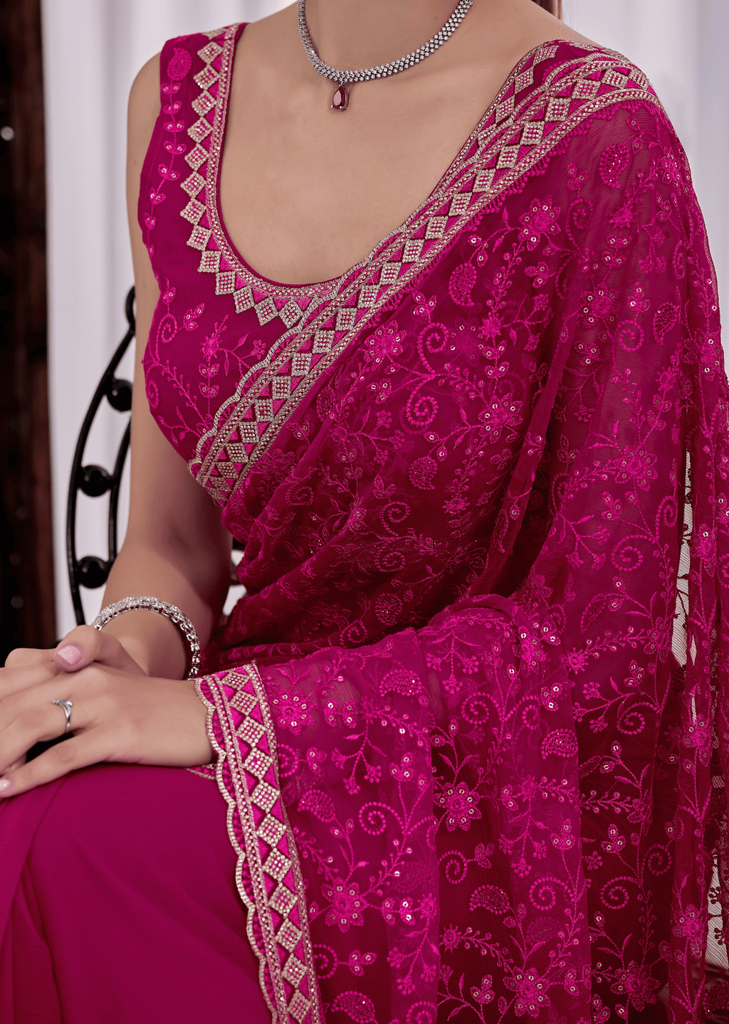 A close-up of a woman wearing a bright magenta pink saree with intricate silver and gold embroidery, featuring a matching embroidered sleeve and blouse.