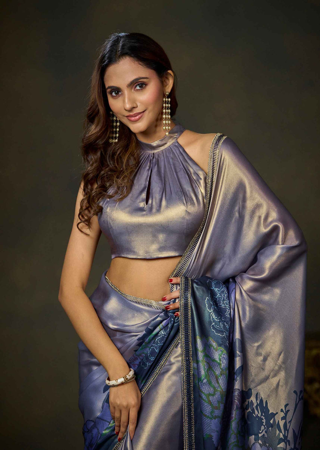 A woman modeling a metallic lavender-blue saree with a matching crop top blouse, draped elegantly against a dark studio background.