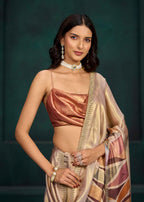 A woman modeling a metallic champagne-gold satin crop top and a matching draped saree with geometric stripes in beige, pink, and gold, set against a dark green background.