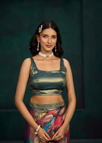 A woman modeling a metallic olive green crop top and a multicolored printed skirt against a dark green studio background.